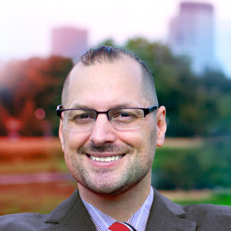 Image of Eric M. Kelsey, Minnesota, a man who is smiling and wearing glasses, a gray suit, and a red tie.